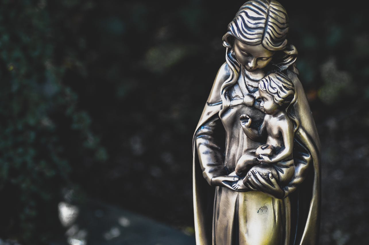 Close-up of a bronze Virgin Mary and Child statue with a blurred background.