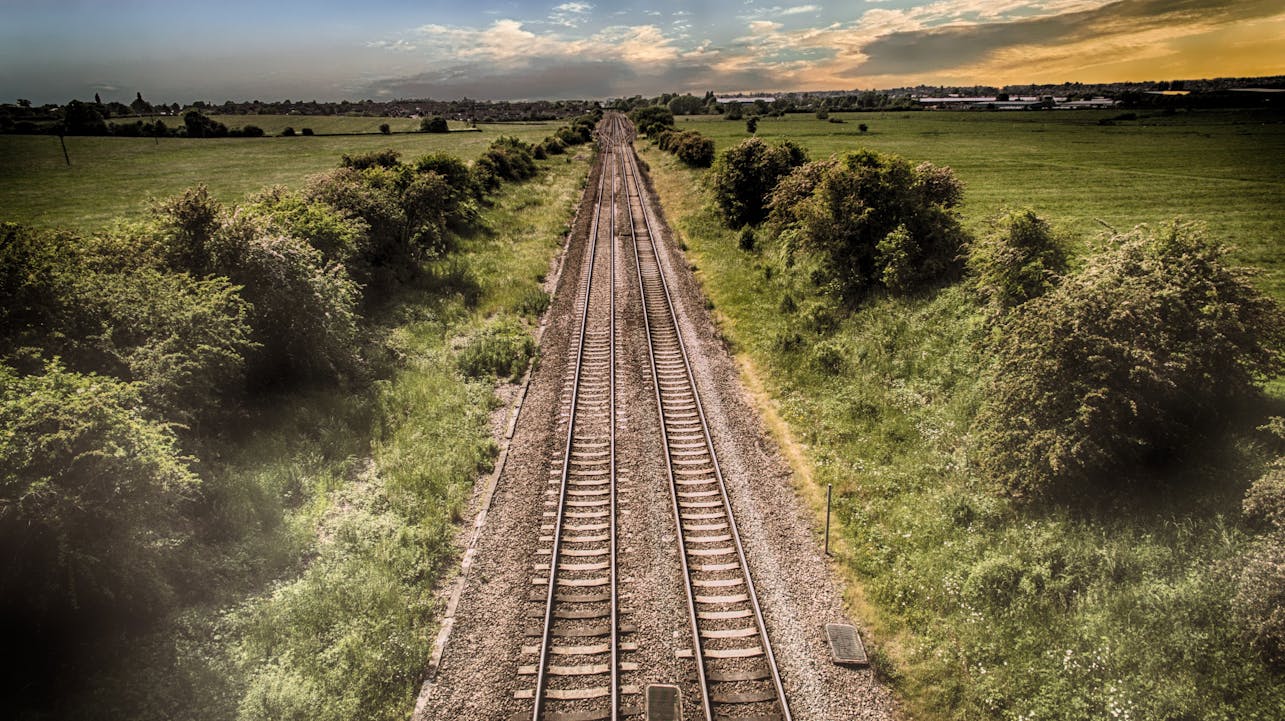 Aerial view of railway tracks through green countryside at sunset, illustrating travel and nature.