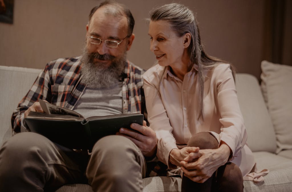 A joyful elderly couple sitting on a couch, reminiscing over a photo album indoors.