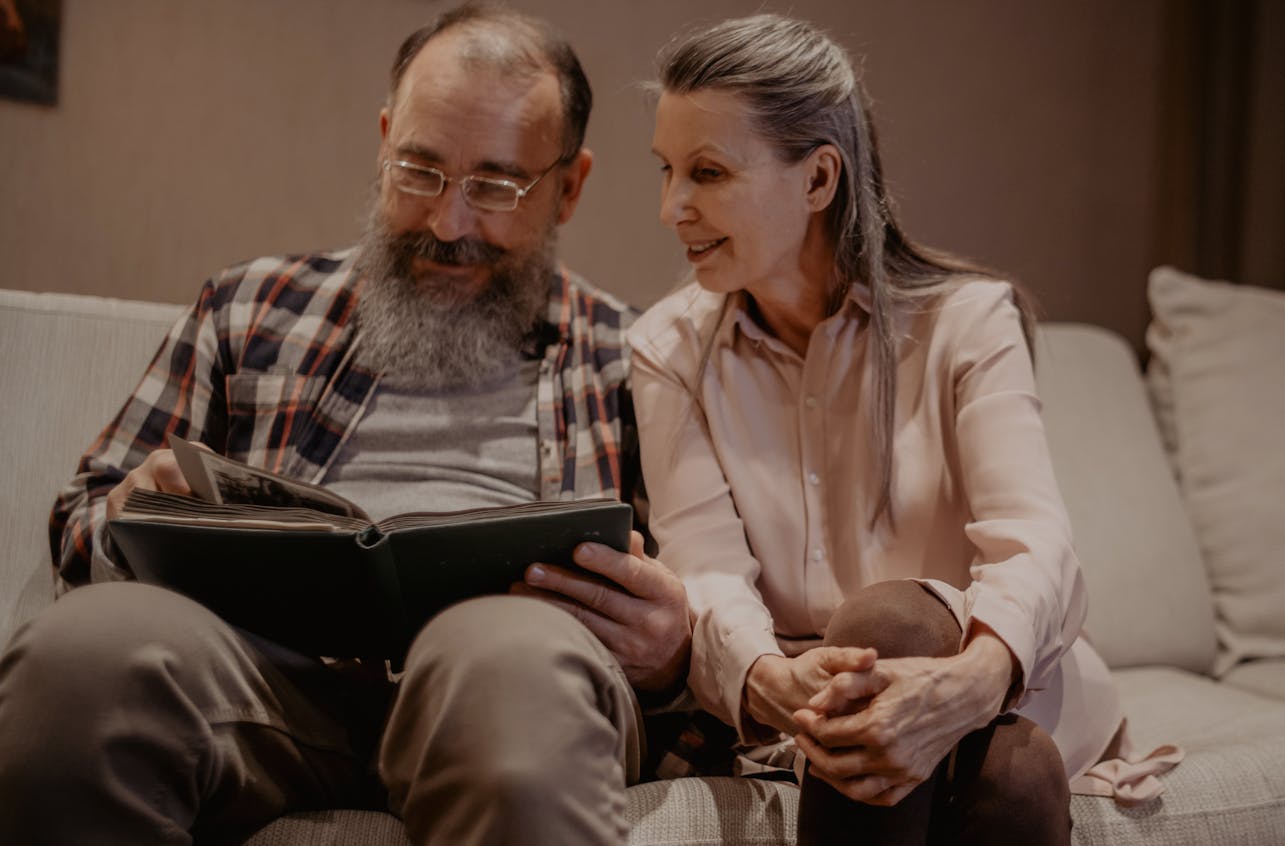 A joyful elderly couple sitting on a couch, reminiscing over a photo album indoors.