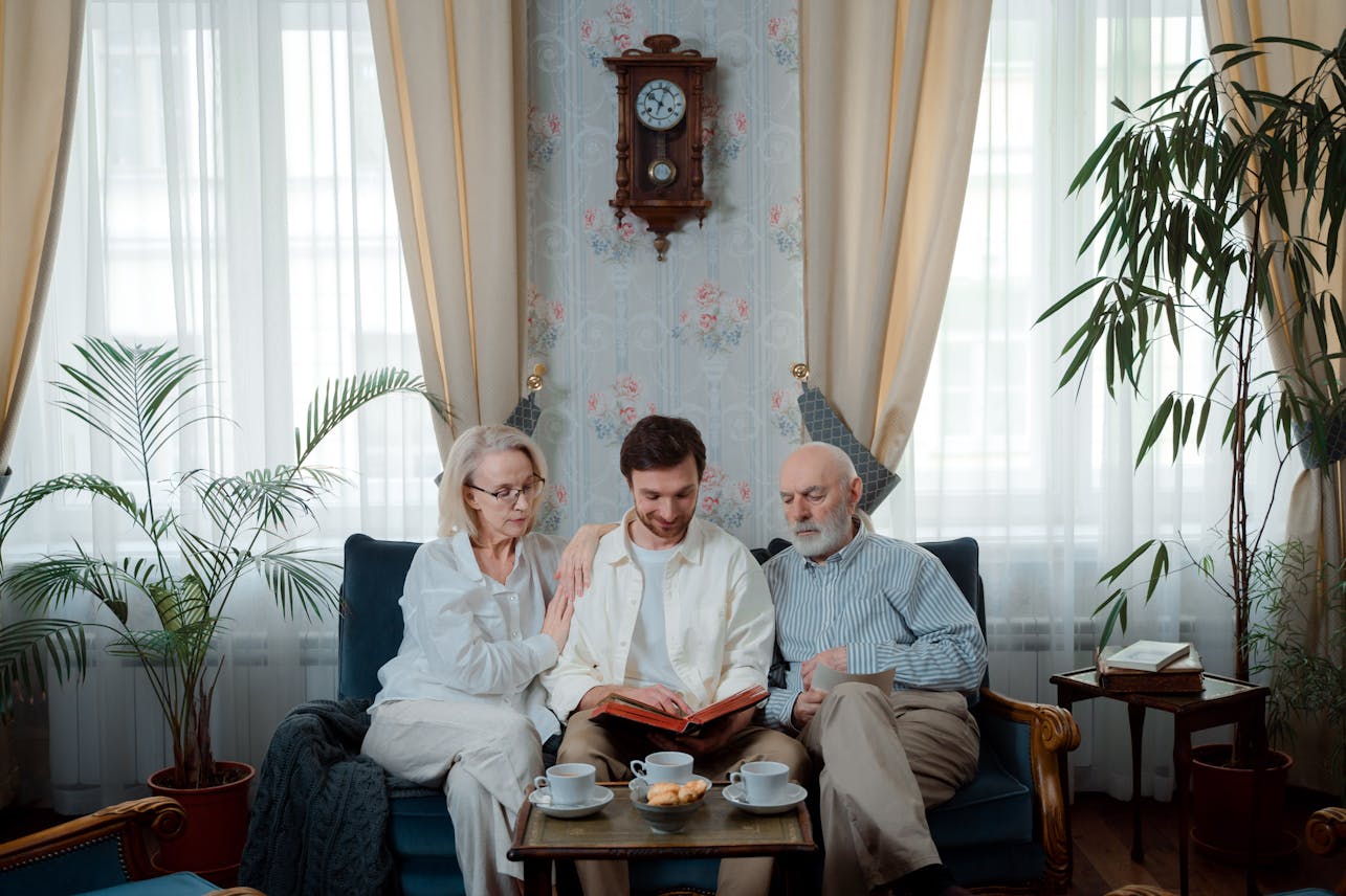 Elderly couple with son enjoying a photo album at home, sharing memories.