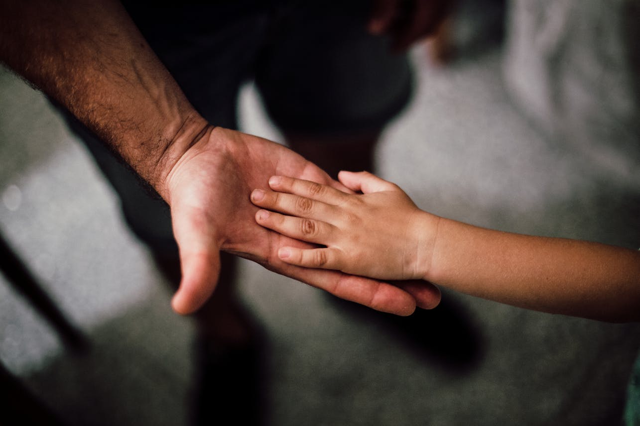 Frieden mit den Ahnen schließen Close-up of a child's hand resting gently on a man's hand, symbolizing love and support.