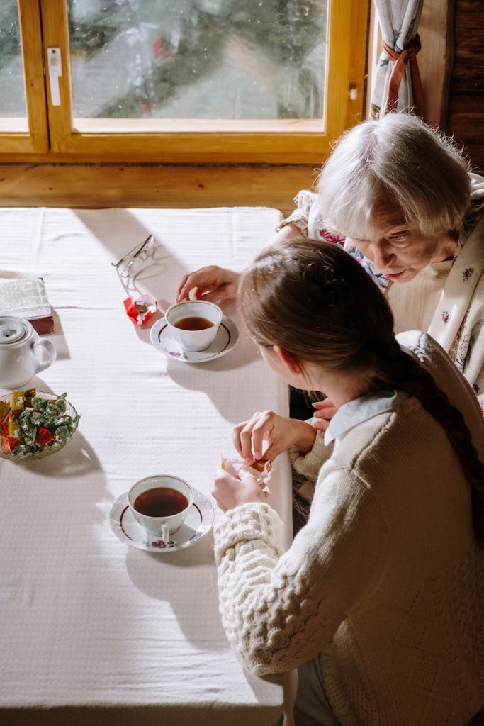 A heartwarming moment of a grandmother and granddaughter sharing tea indoors on a sunny day.
