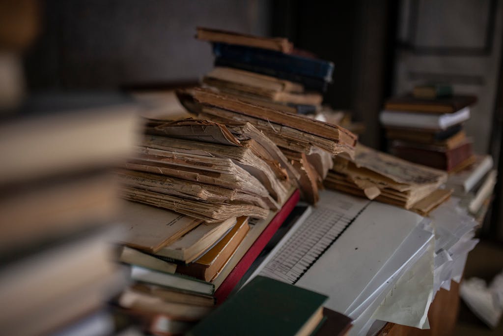 Atmospheric close-up of a stack of antique books with yellowed pages in a dimly lit library.