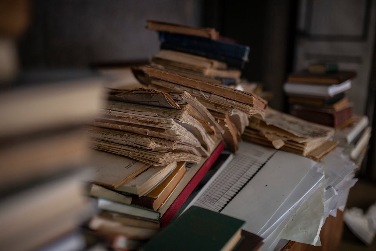Atmospheric close-up of a stack of antique books with yellowed pages in a dimly lit library.